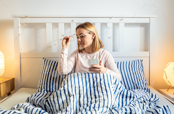 Smiling lady makes use of her cell phone in bed in the morning.