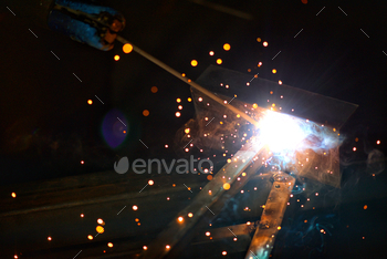 Sparks and bokeh flashes of sunshine against a awful background as an industrial metalworker works