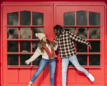 smiling multiracial couple having fun exterior, pink doors on the background