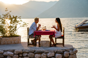 Couple in fancy drinking champagne wine on romantic dinner at sunset on the seaside