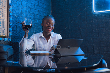 Murky woman working with a digital pill and a notebook in a pub whereas she is ingesting wine