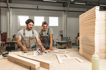 Two younger males carpenters making furniture in warehouse of wood manufacturing facility