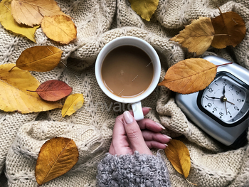 Overhead Sight Of Feminine Hand Preserving Espresso Cup Surrounded By Yellow  Autumn Leaves And Fear Clock