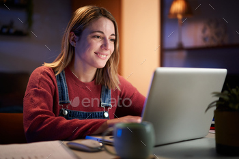 Young Caucasian girl working smiling from home in front of computer computer. College college students of us.