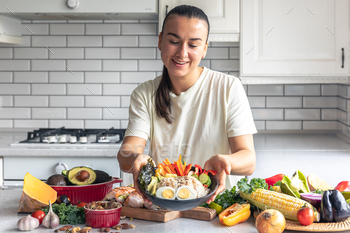 A young lady with a plate of vegetables, rice and eggs in the kitchen.