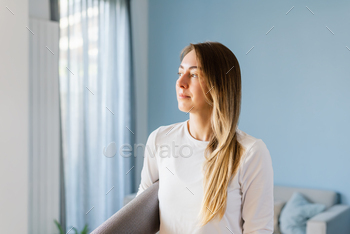 Portrait of a young lady in sports clothing with a yoga mat within the comfy lounge. Reproduction house.