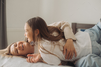 Pack up cheery mother cuddles tickles cramped cute daughter lying in bed.