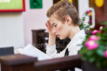 clear girl with a book sits at a desk in a cafe and crimson plant life spring makeup