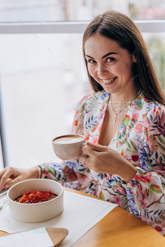 Younger pleasing current lady ingesting coffee while sitting in restaurant and eating tasty dish