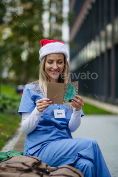 Nurse with christmas hat on head studying christmas card from youngster patient. Working in hospital on