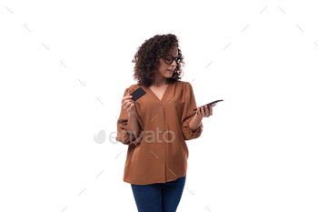 younger slim lady with curly haircut retaining smartphone and plastic card with mockup