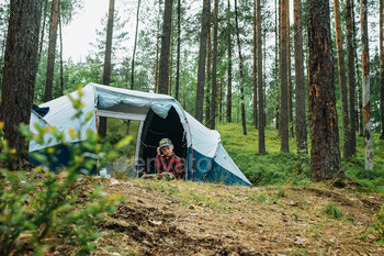 cute caucasian boy carrying hat sitting interior a obedient touristic tent. Household tenting idea