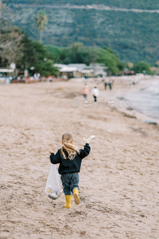 Little woman in gloves with a garbage web runs alongside the seaside. Again achieve out about