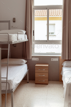 A orderly and minimalistic hostel room with a bunk mattress, white bedding, and  little wooden bedside desk