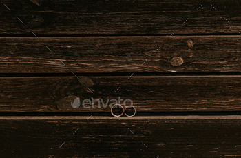 pair gold wedding ceremony engagement rings positioned on darkish brown picket striped timber plank background