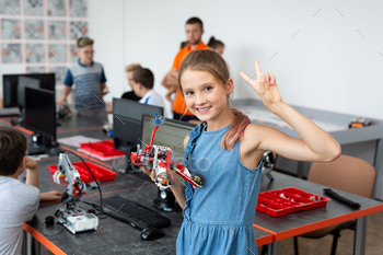 Portrait of a choolgirl lady in a robotics class, she holds a robotic assembled from plastic formulation.