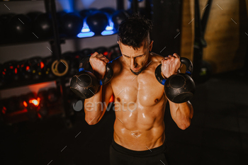 A muscular shirtless sportsman is lifting kettlebells on the gymnasium.