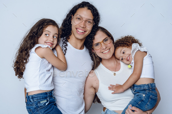 studio portrait of younger happy latin household, mother and pa with two daughters smiling fortunately.