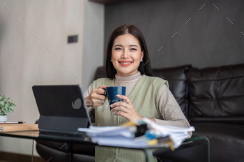 Contented youthful asian freelance trade girl sitting on the ground at dwelling engaged on digital pill