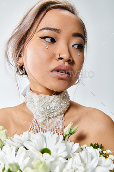 charming asian woman in her 20s with white plants taking a peep to side on mild background