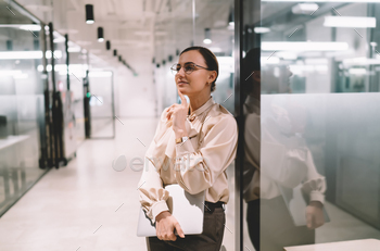 Thoughtful female with pc private pc standing come glass wall at work