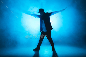 Male smash dancer performs on blue neon stage his expressive dance, mild flare