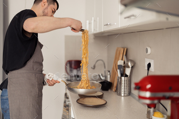 Man getting ready spaghetti in a latest kitchen at residence