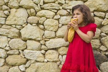 Restricted girl in a crimson costume having fun with a baguette towards a stone wall backdrop