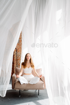 A younger feminine yogi in white clothes sits within the lotus preserve of dwelling on a chair towards a background of