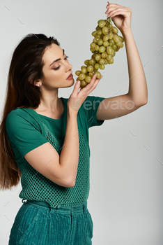 Girl in Inexperienced Attire Smells a Bunch of Grapes