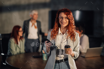 Businesswoman at boardroom holding cellphone and smiling at digicam on assembly