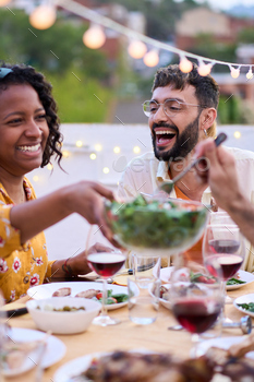 Smiling African American girl sitting at desk passing salad to happy friends at meal match outside