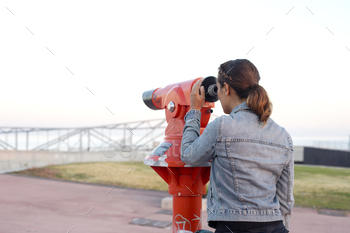 Lady looking through a crimson telescope at an open air commentary deck.