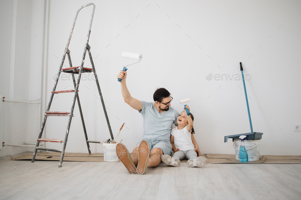 Youthful father and his cramped blonde sterling-looking out woman daughter with wall paint rollers sitting on the bottom