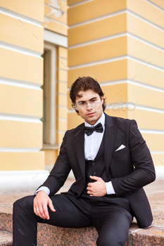 Assured businessman man in tuxedo sitting outdoors, sturdy making an attempt at digicam