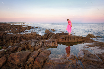 Swish younger woman in purple costume standing on the rock with reflecions throughout the water at Wild atlanti