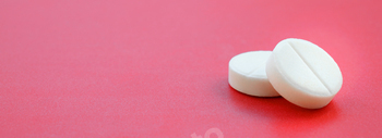 A pair of white tablets lie on a shiny crimson background floor