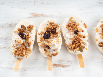 Home made greek yogurt popsicles with granola on white picket board