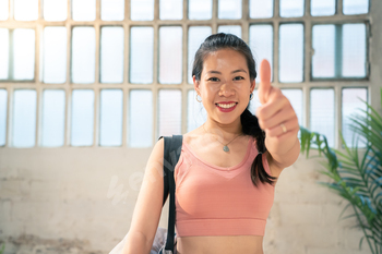 A lady enthusiastically affords a thumbs up stamp whereas holding her yoga mat