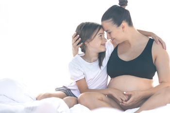 A pregnant lady and her teenager daughter are sitting on the mattress.