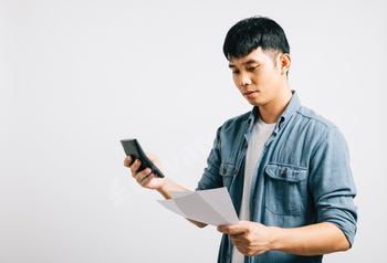 A younger man, remoted on white, seems sad, drained, and strained as he holds a paper and calculator