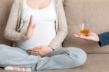 Pack up of pregnant woman sitting on the couch refuses to drink whisky and makes stop gesture