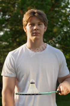 Youthful man sustaining white badminton shuttlecock and badminton racket. Summer season sports activities actions sport. Outside.