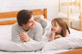 Cheerful daddy and his liitle woman laying in mattress