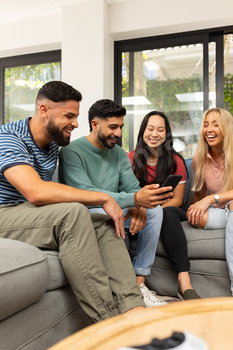 varied pals sitting on sofa, laughing and trying at smartphone collectively