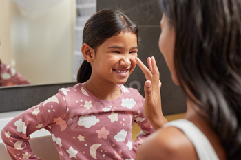 Mom making train of moisturizing lotion on daughter face