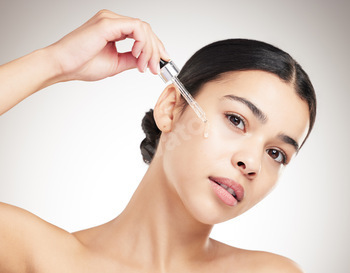 Portrait of a youthful blended dash girl making use of oil to her face whereas standing in opposition to a grey studio