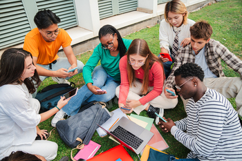 Quite a few neighborhood of college college students sitting on the college campus yard, the bid of cellphones and reviewing