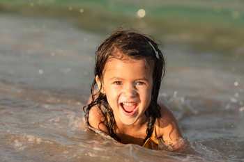 Summer time portrait of totally completely satisfied toddler woman on the shore laughing and taking a look at digicam