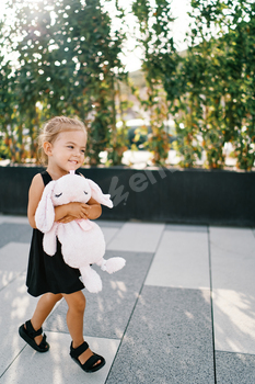 Tiny smiling woman walks hugging a pleasurable purple toy hare